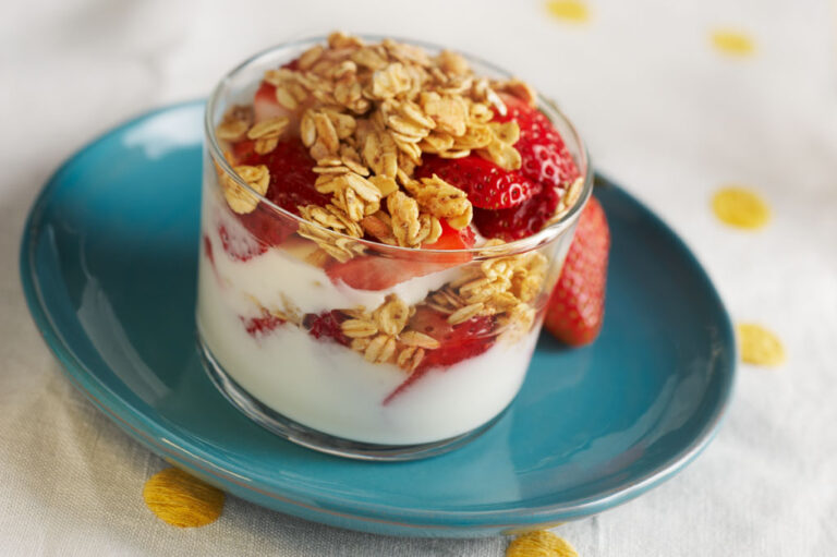Clear cup with yogurt, fruit, and granola on top of a blue plate.