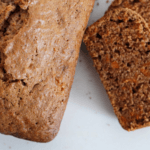 Two slices of carrot bread next to a carrot bread loaf on a white surface.