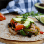 Chicken fajitas topped with avocado slices on a whole wheat tortilla.