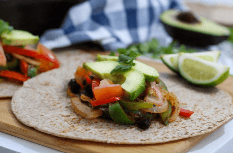 Chicken fajitas topped with avocado slices on a whole wheat tortilla.