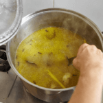 A person mixing chicken stock in a large pot