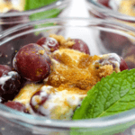 Glass bowl filled with yogurt, grapes, mint, and ginger topping.