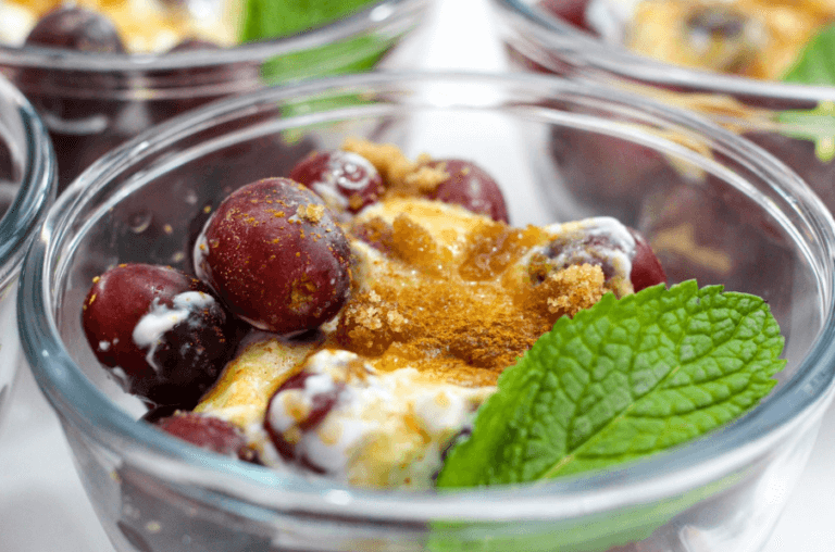 Glass bowl filled with yogurt, grapes, mint, and ginger topping.