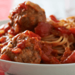 Spaghetti and meatballs in a white bowl.