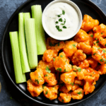 Buffalo Roasted Cauliflower on a black plate with ranch and celery sticks