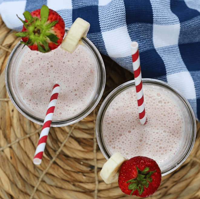 Two glasses of oatmeal, strawberry, banana smoothies garnished with a strawberry and banana with a red- and white-striped straw.