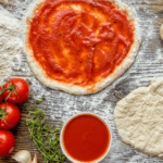 Pizza dough, sauce, flour, and tomatoes on a wood table
