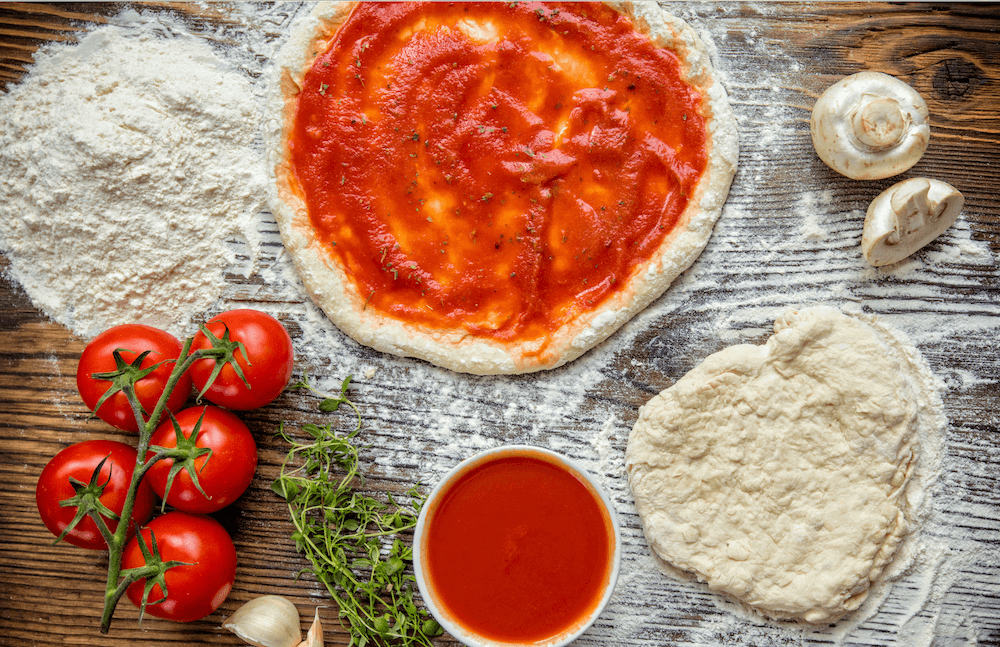 Pizza dough, sauce, flour, and tomatoes on a wood table