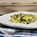 A white plate with a single slice of spinach-rice casserole on top of a blue and white checkered cloth.