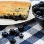 Blueberry cobbler on a white plate next to a bowl of blueberries.