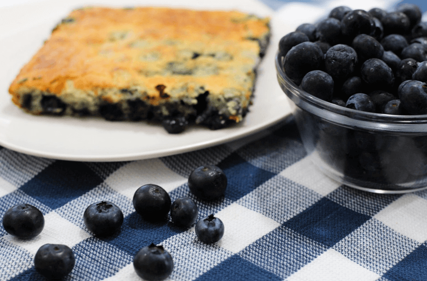 Blueberry cobbler on a white plate next to a bowl of blueberries.