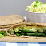 Egg salad in a pita bread pocket with greens and white dish of egg salad in the background.
