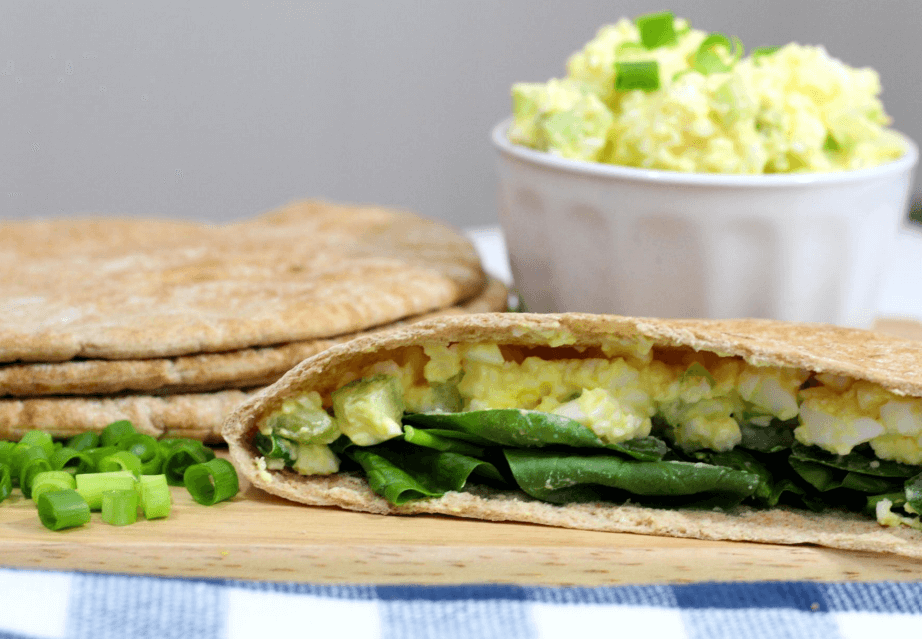 Egg salad in a pita bread pocket with greens and white dish of egg salad in the background.
