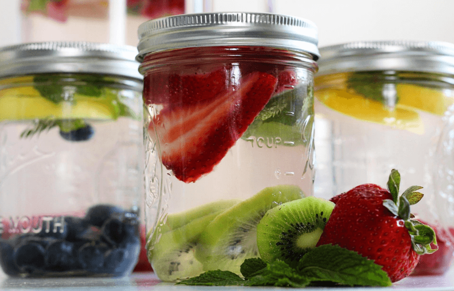 Three glass jars filled with water and different kinds of fruit.