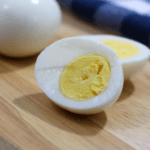 One hard-boiled egg cut in half on a wooden surface with two hard-boiled eggs in the background.