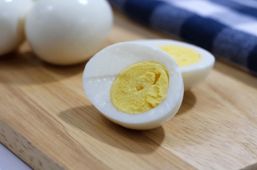 One hard-boiled egg cut in half on a wooden surface with two hard-boiled eggs in the background.