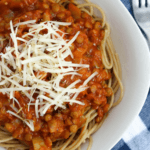 A dish of spaghetti noodles topped with lentil spaghetti sauce and shredded cheese.