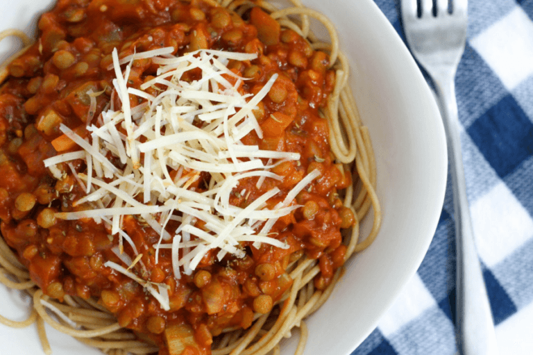 A dish of spaghetti noodles topped with lentil spaghetti sauce and shredded cheese.