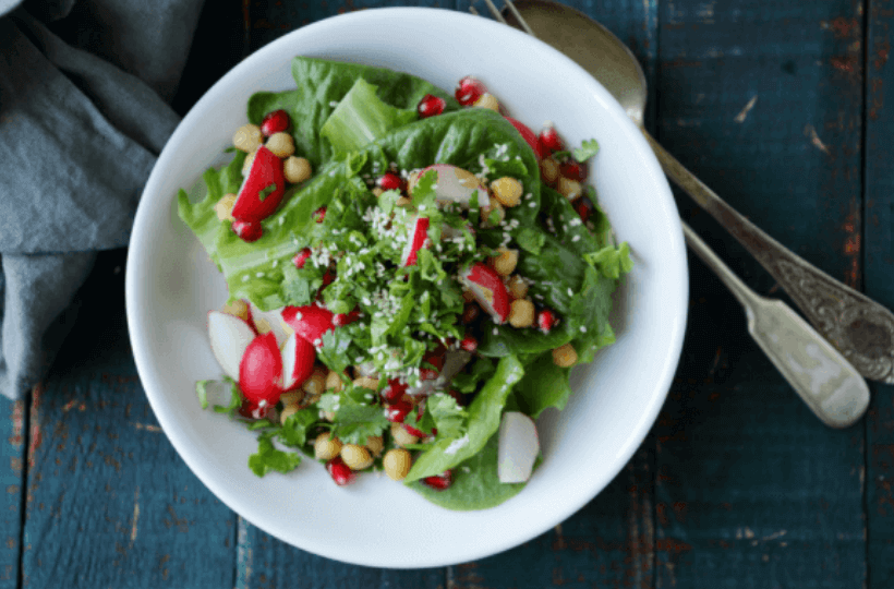 A white bowl filled with a spring salad of lettuce greens and radishes.