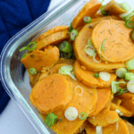 Clear dish of sweet potato salad topped with scallions and apple cider vinaigrette.