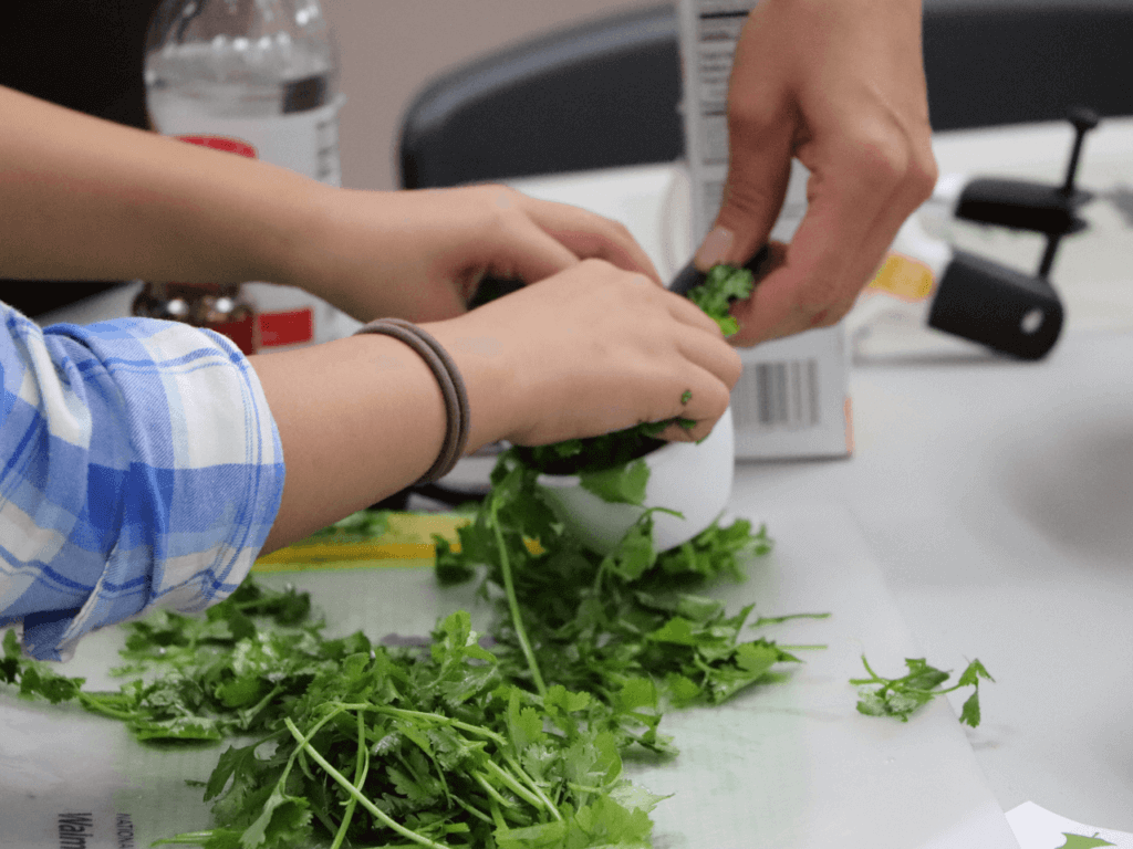 Cooking with Kids a Child and adult chopping green produce on cutting board