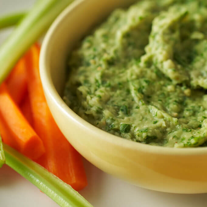 Spicy white bean dip in a yellow bowl with bright orange carrots and lime green celery
