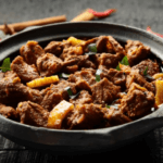 Black skillet filled with curried goat meat and vegetables.