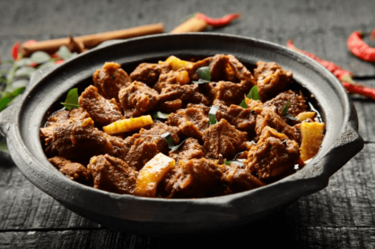 Black skillet filled with curried goat meat and vegetables.