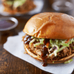 A BBQ beef sandwich topped with shredded lettuce on a white paper napkin.