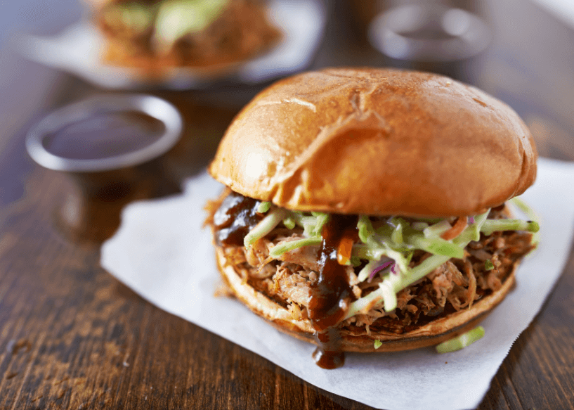 A BBQ beef sandwich topped with shredded lettuce on a white paper napkin.