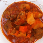 A bright bowl of goat stew in a white bowl.