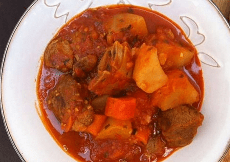A bright bowl of goat stew in a white bowl.