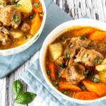 Two bowls of colorful lamb stew with potatoes and carrots with a rustic wooden background.