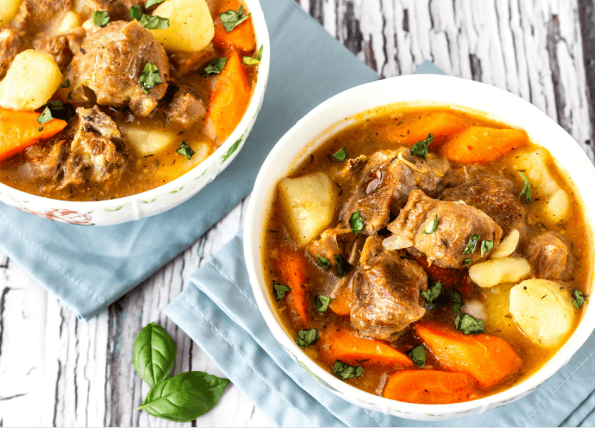 Two bowls of colorful lamb stew with potatoes and carrots with a rustic wooden background.