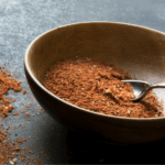 Brown, wooden bowl full of taco seasoning with some of the seasoning dusted outside of the bowl.