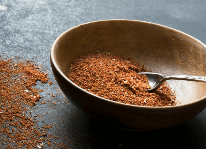 Brown, wooden bowl full of taco seasoning with some of the seasoning dusted outside of the bowl.