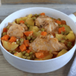 White pan filled with rabbit stew with carrots, peas, and potatoes.