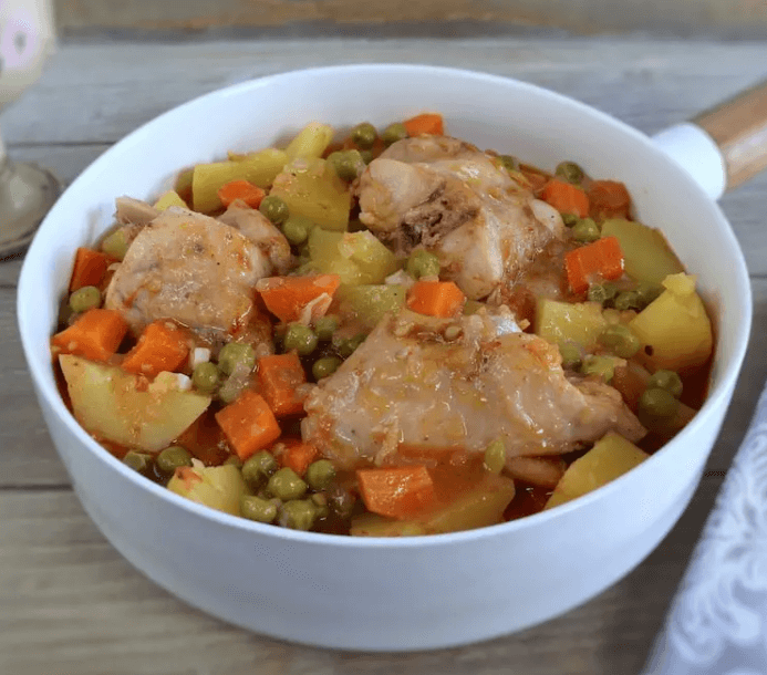 White pan filled with rabbit stew with carrots, peas, and potatoes.