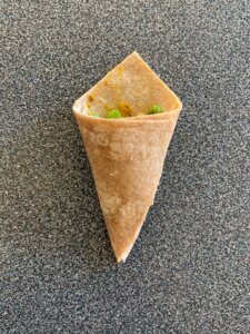 A triangle-shaped piece of dough with two corners folded on top and filled with peas