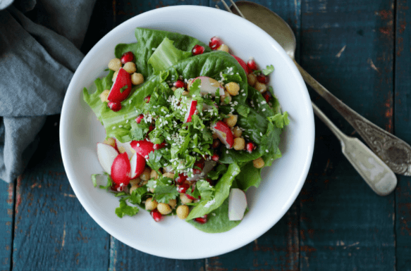 Colorful spring salad with greens and radishes in a white bowl.