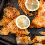 Baked catfish with Cajun seasoning and lemon slices.