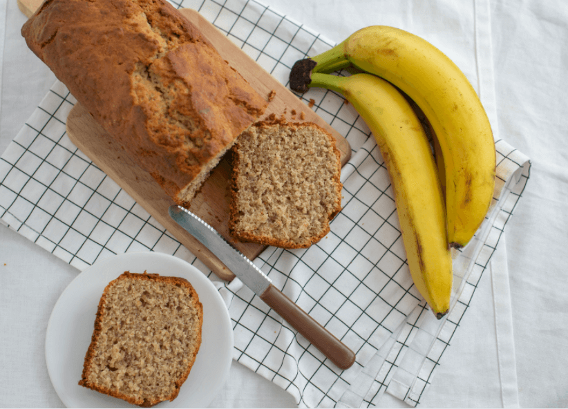 One loaf of banana bread with two cut pieces next to two bananas.