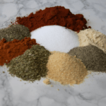 Piles of spices that make up Cajun seasoning on a marbled surface.
