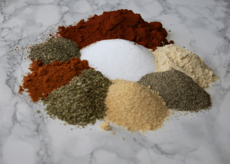 Piles of spices that make up Cajun seasoning on a marbled surface.