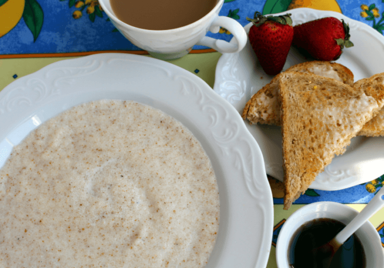 A white bowl of farina with two slices of toast, strawberries, and coffee on the side.