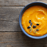 A dark bowl filled with pumpkin farina and a garnish on a wooden surface.