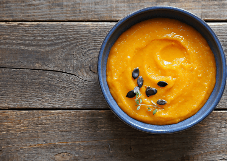 A dark bowl filled with pumpkin farina and a garnish on a wooden surface.