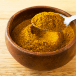 A wooden bowl with ras el hanout seasoning on a wooden surface.