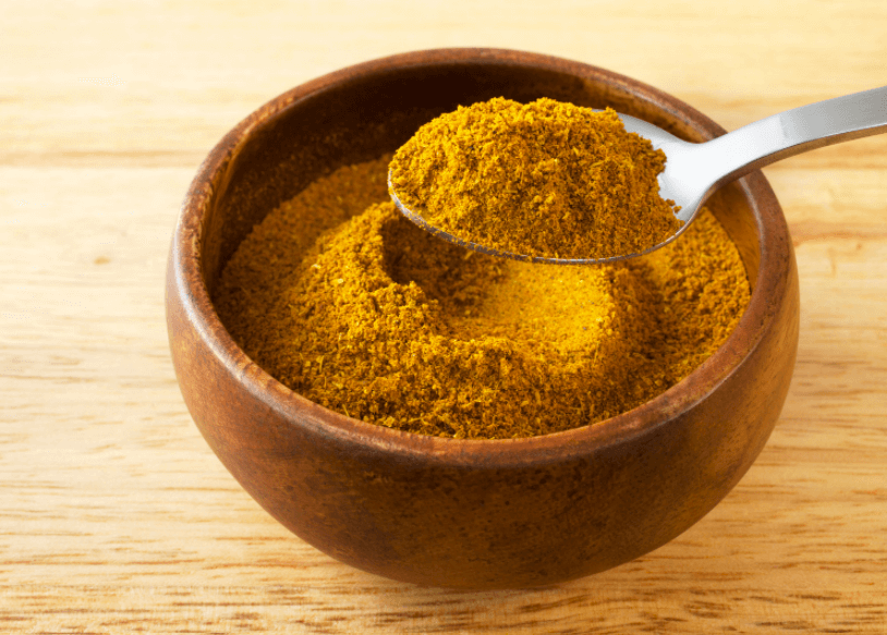 A wooden bowl with ras el hanout seasoning on a wooden surface.