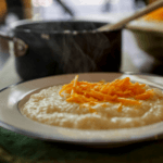 A shallow bowl of savory farina topped with bright orange shredded cheese and a saucepan in the background.